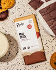 flatlay of oat milk chocoate bar with the bar, a cookie, and a glass of milk surrounding the bar