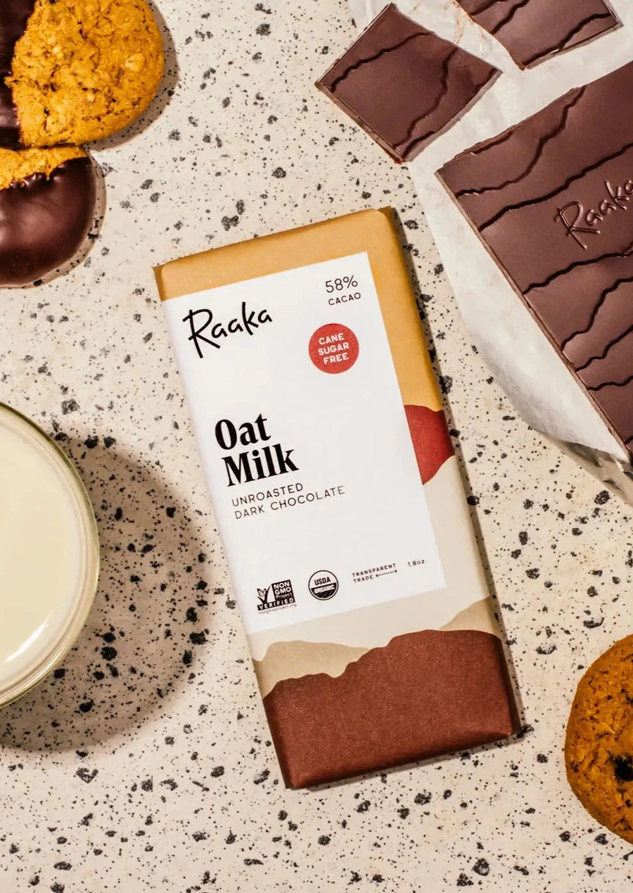 flatlay of oat milk chocoate bar with the bar, a cookie, and a glass of milk surrounding the bar