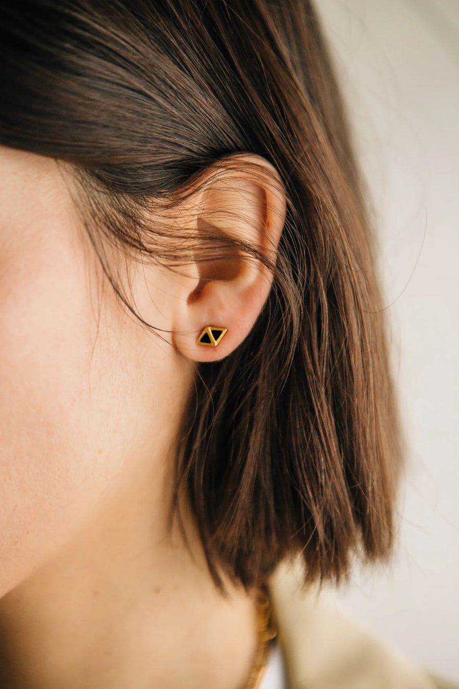 close-up of models ear with a diamond shaped gold vermeil stud earring on it.