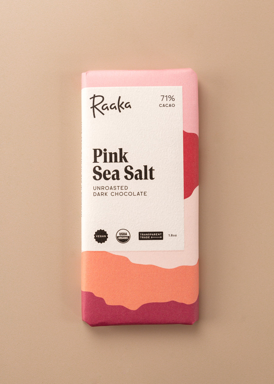 flatlay of an unroasted dark chocolate bar ‘pink sea salt’ by Raaka. Cover is layers of colors in a variety of cream, pinks and orange
