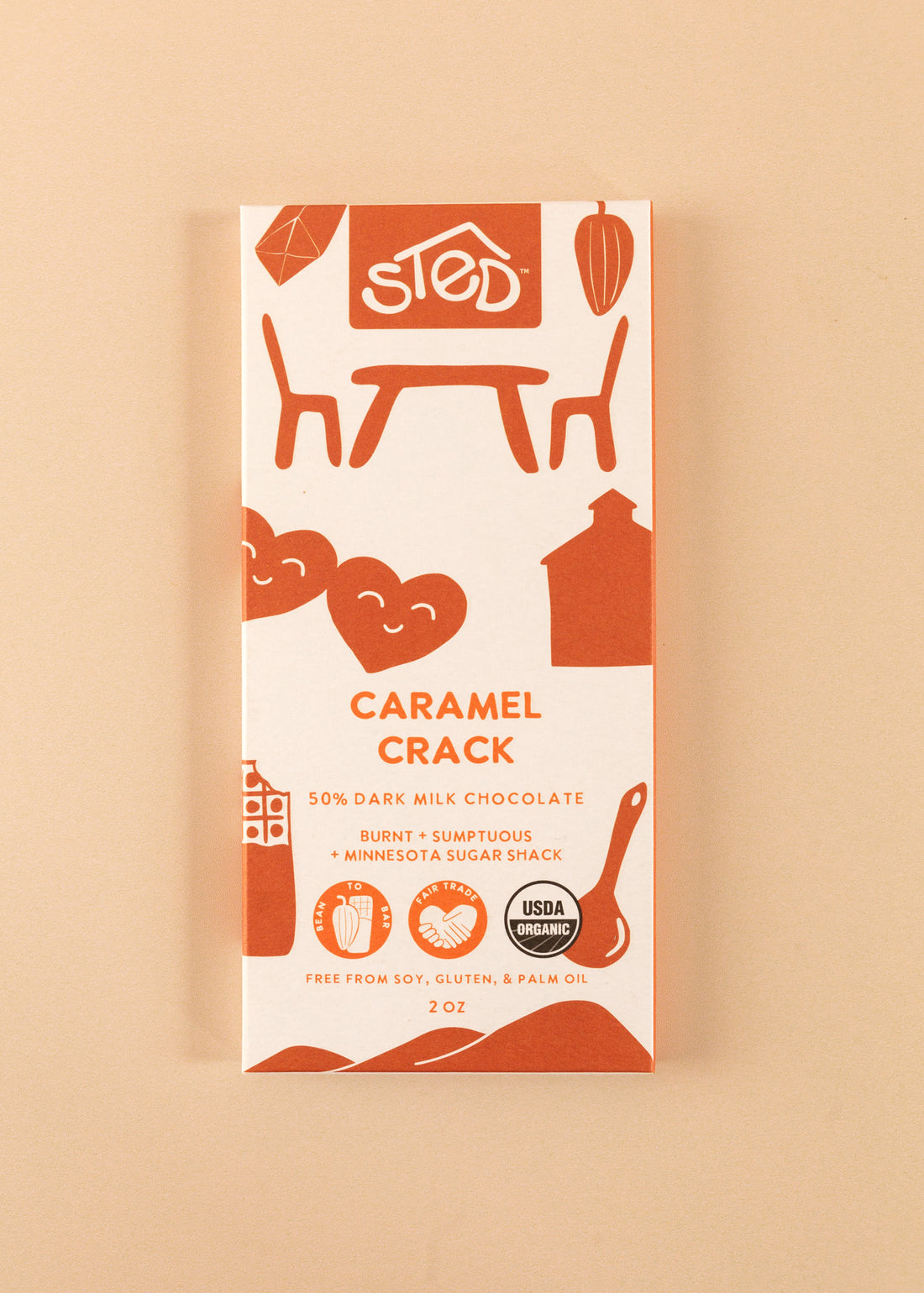 flatlay of the cover of a 50% dark milk chocolate bar by Sted. A white cover with deep orange artwork throughout, named ‘caramel crack’