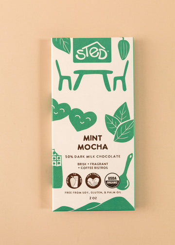 flatlay of the cover of a 50% dark milk chocolate bar by Sted. A white cover with green artwork throughout, named ‘mint mocha’