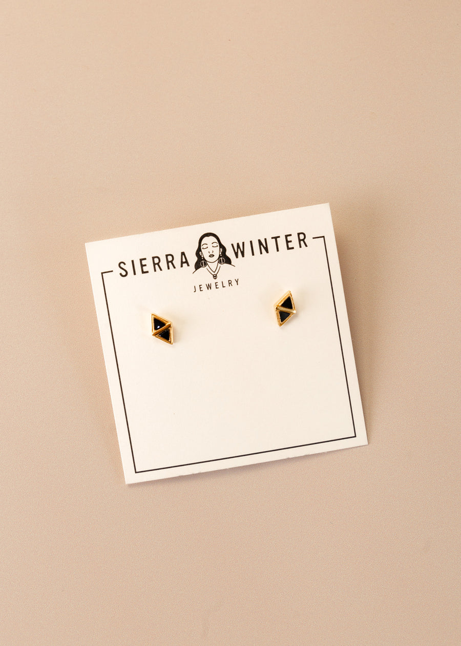 flatlay of a jewelry card stating "sierra winter jewelry" with two diamond-shaped gold studs with black onyx in the center on it.
