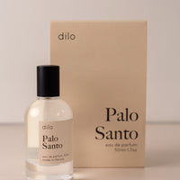 Bottle of perfume by dilo, with a cream label on the front stating “palo Santo. eau de parfum, 50 ml. made in the usa" with the cream box that it comes in in the background