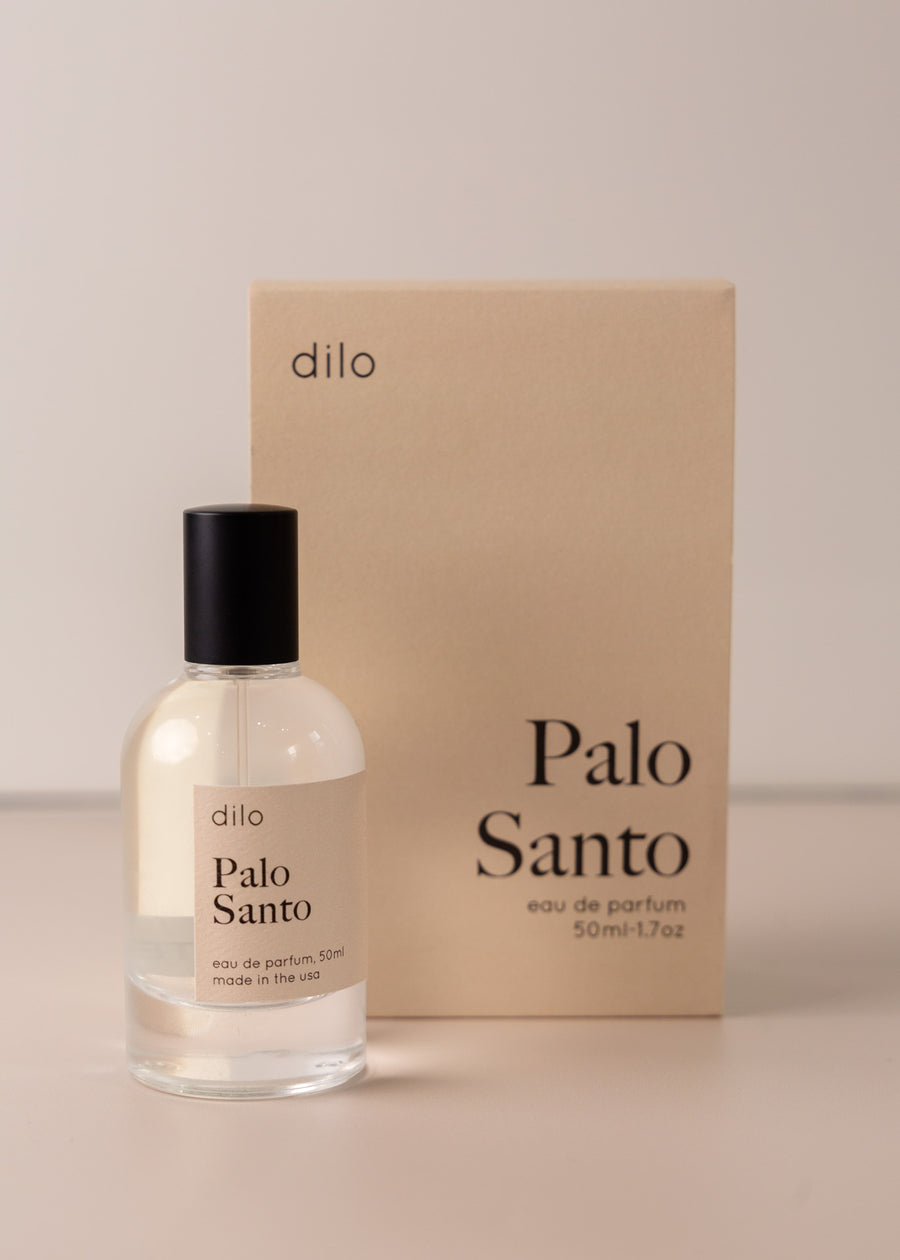Bottle of perfume by dilo, with a cream label on the front stating “palo Santo. eau de parfum, 50 ml. made in the usa" with the cream box that it comes in in the background