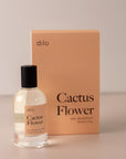 Bottle of perfume by dilo, with a pink label on the front stating “cactus flower. eau de parfum, 50 ml. made in the usa" with the pink box that it comes in in the background