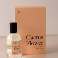 Bottle of perfume by dilo, with a pink label on the front stating “cactus flower. eau de parfum, 50 ml. made in the usa" with the pink box that it comes in in the background