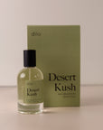 Bottle of perfume by dilo, with a green label on the front stating “desert kush. eau de parfum, 50 ml. made in the usa" with the green box that it comes in in the background