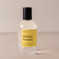 Bottle of perfume by dilo, with a yellow label on the front stating "hinoki sesame. eau de parfum, 50 ml. made in the usa"