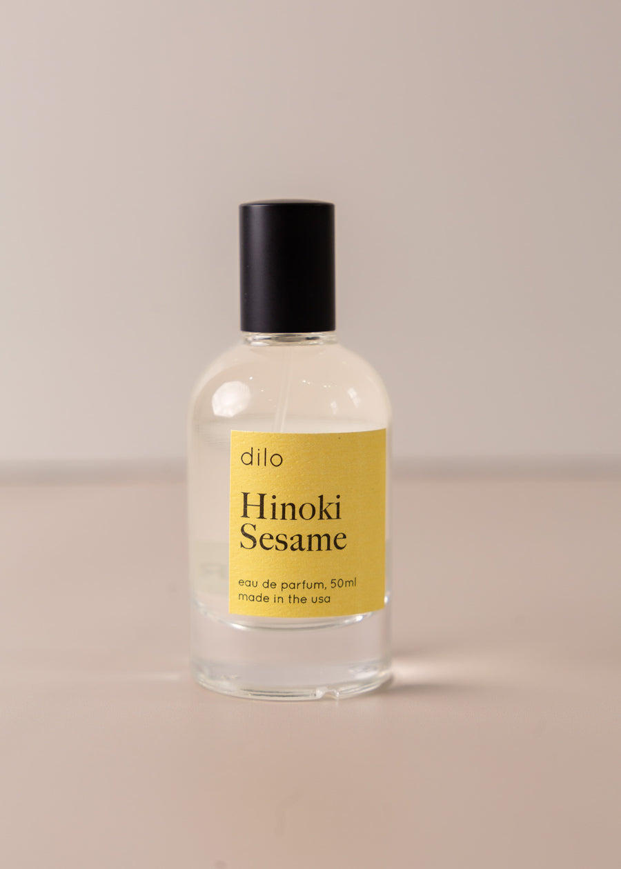 Bottle of perfume by dilo, with a yellow label on the front stating "hinoki sesame. eau de parfum, 50 ml. made in the usa"