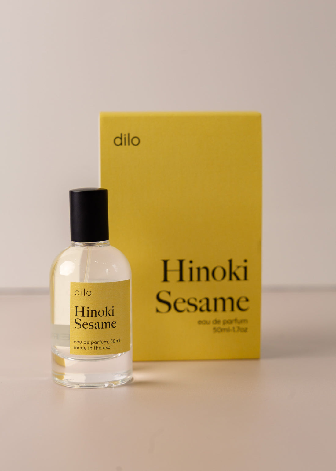Bottle of perfume by dilo, with a yellow label on the front stating "hinoki sesame. eau de parfum, 50 ml. made in the usa" with the yellow box that it comes in in the background