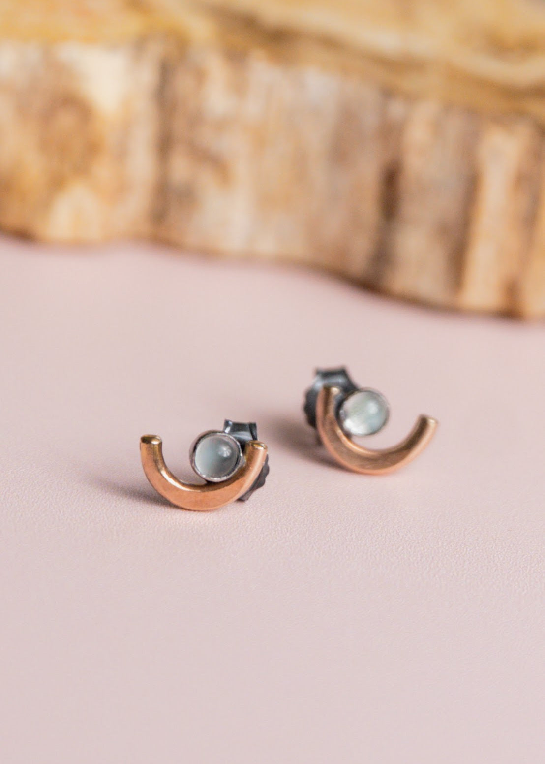 Pair of crescent moon earrings by Claire Sommers Buck on soft pink background