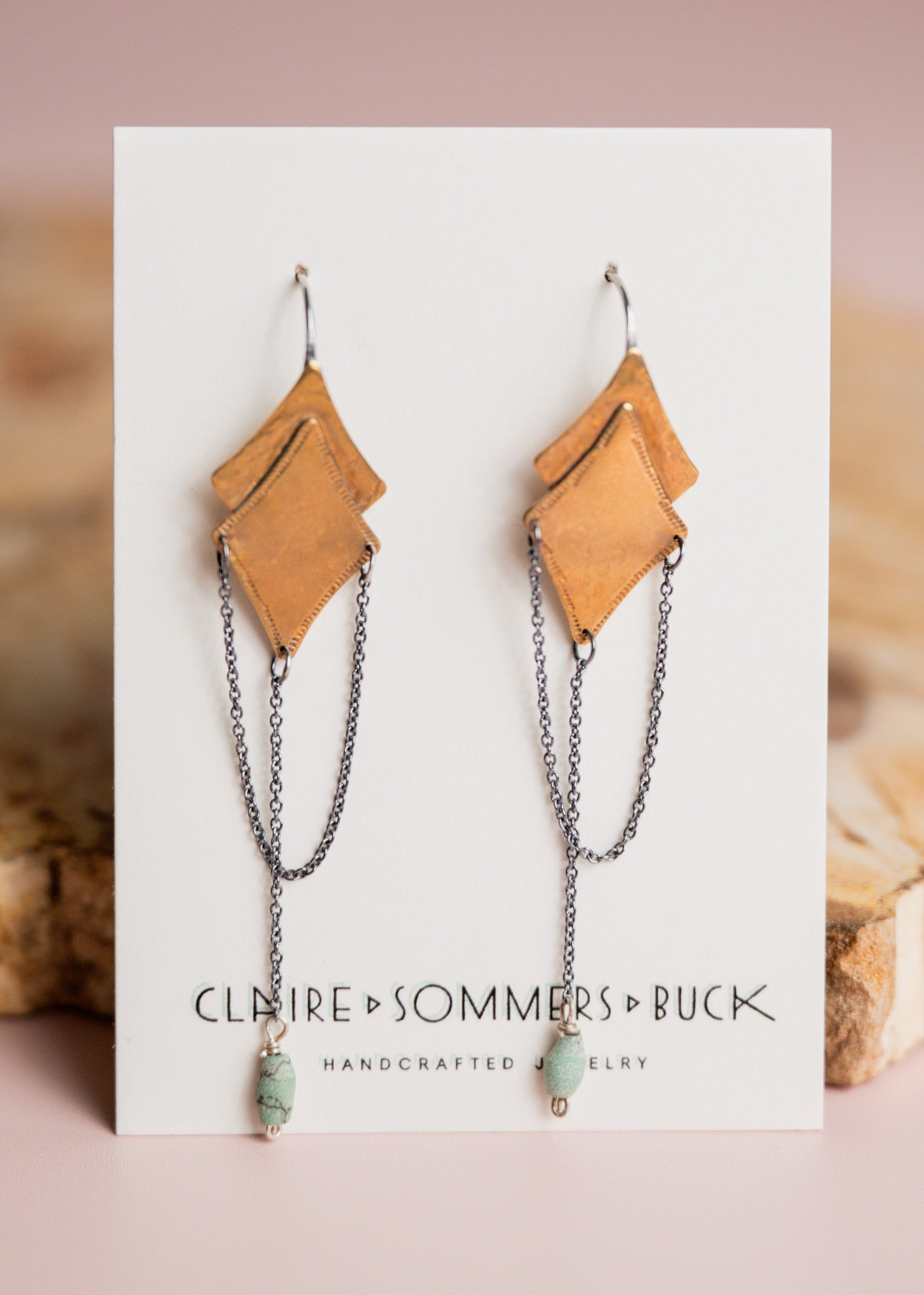 Pair of gold and silver Morning Star earrings by Claire Sommers Buck shown on white card with a pink background