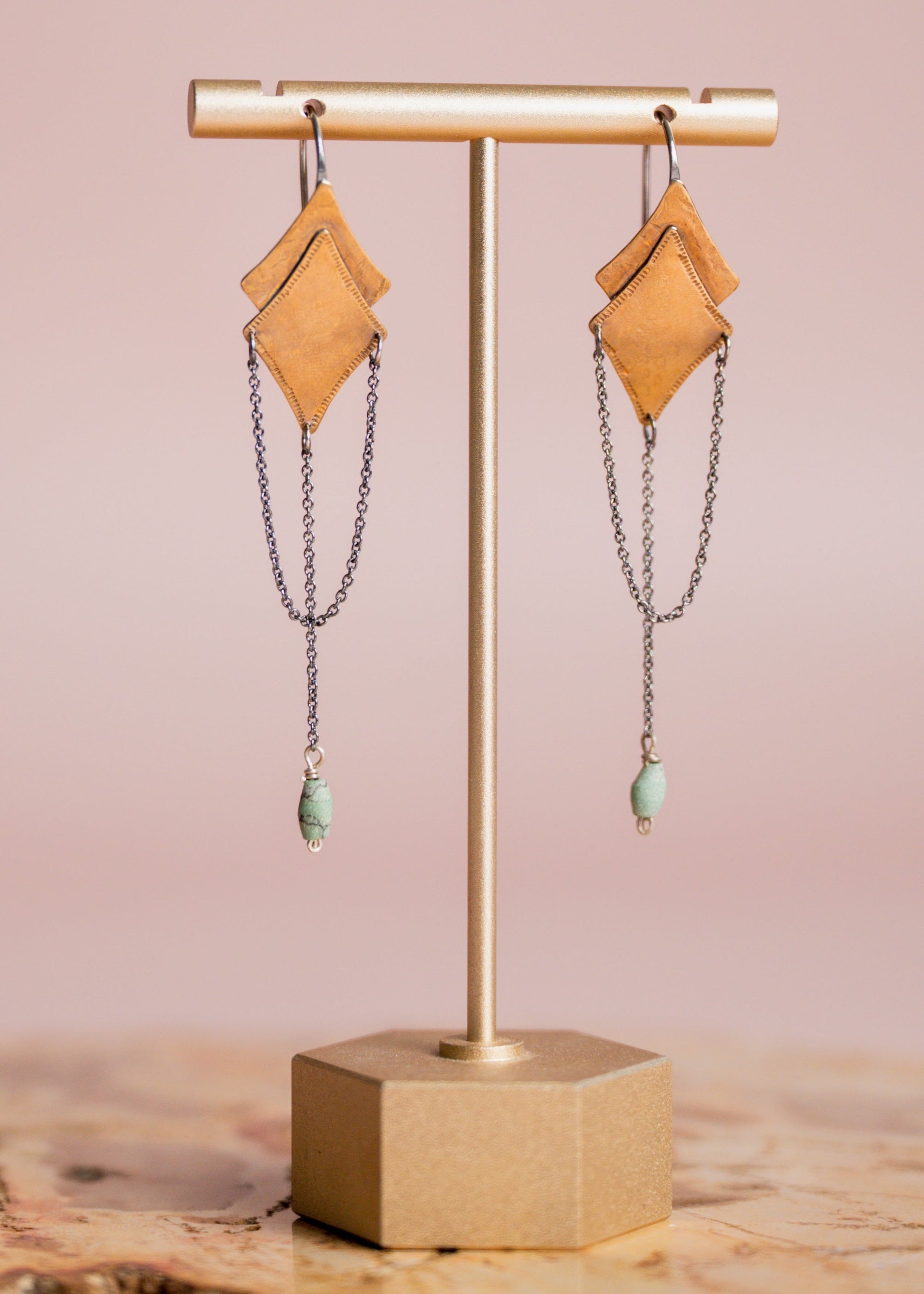 Pair of gold and silver Morning Star earrings by Claire Sommers Buck shown on stand with a pink background