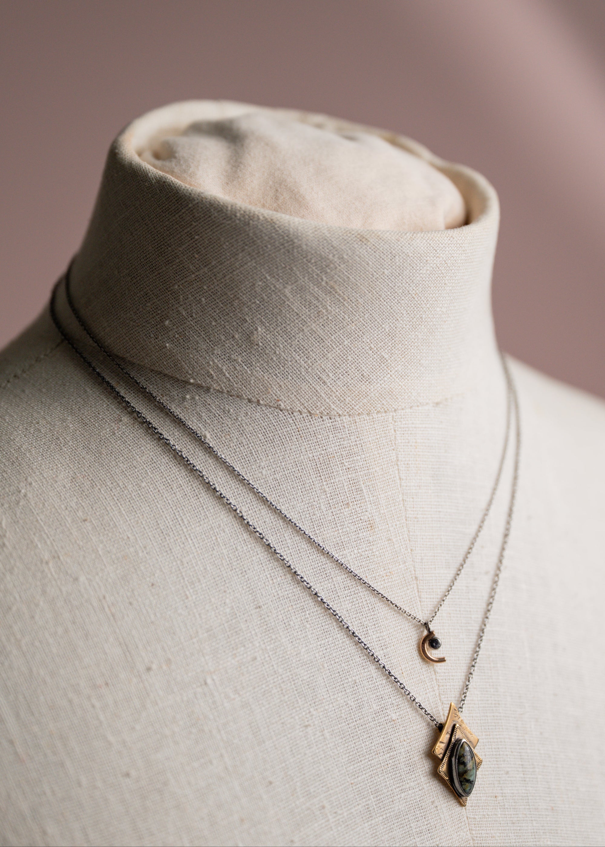 Crescent moon necklace layered with  pendant necklace on a mannequin bust against a neutral background