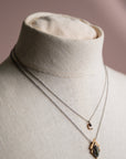Crescent moon necklace layered with  pendant necklace on a mannequin bust against a neutral background