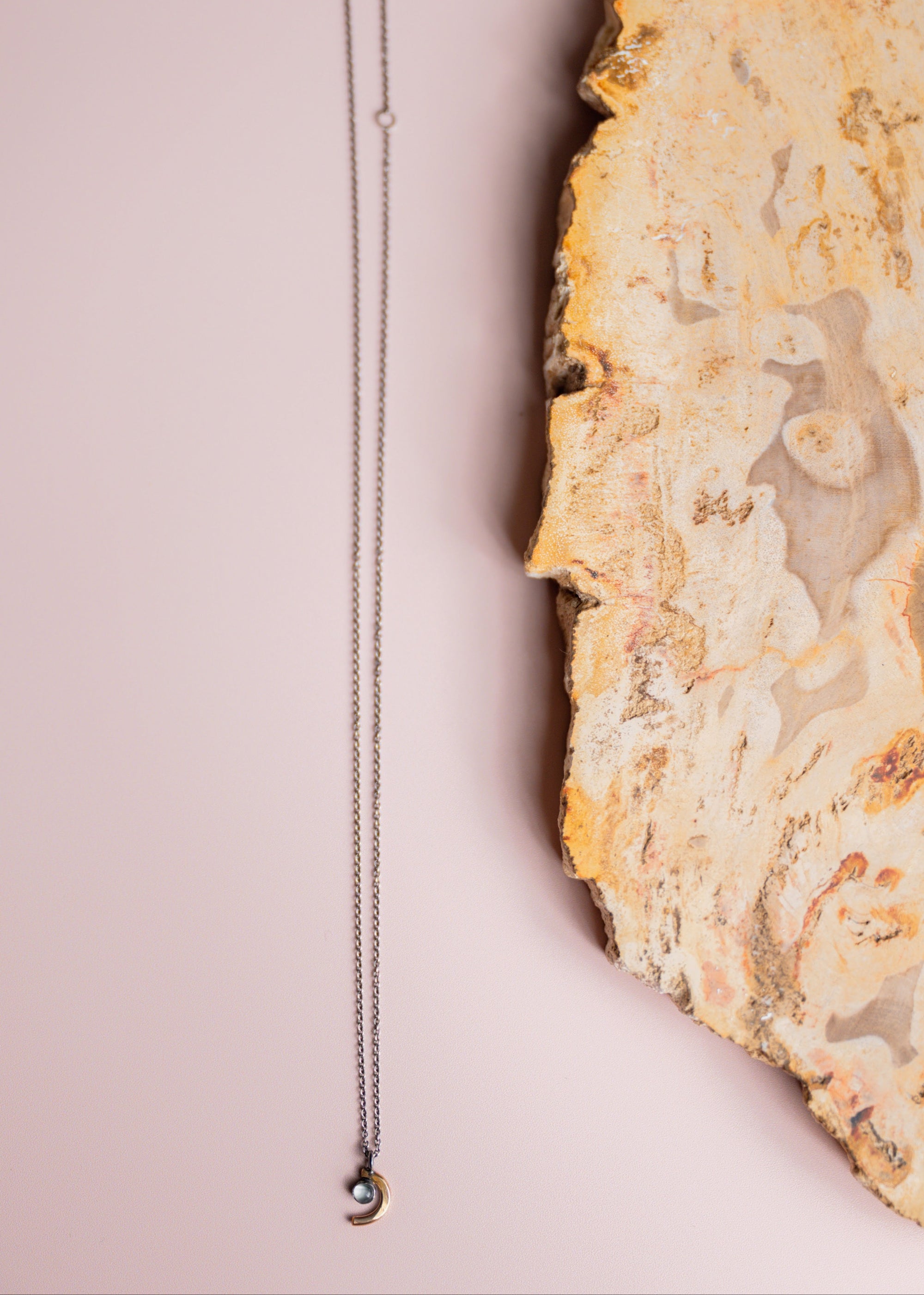 Crescent moon necklace by Claire Sommers Buck on a textured stone surface
