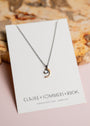 Crescent moon pendant by Claire Sommers Buck against a textured background