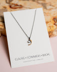 Crescent moon pendant by Claire Sommers Buck against a textured background