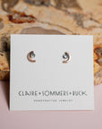 Pair of crescent moon earrings by Claire Sommers Buck branded card against a stone background