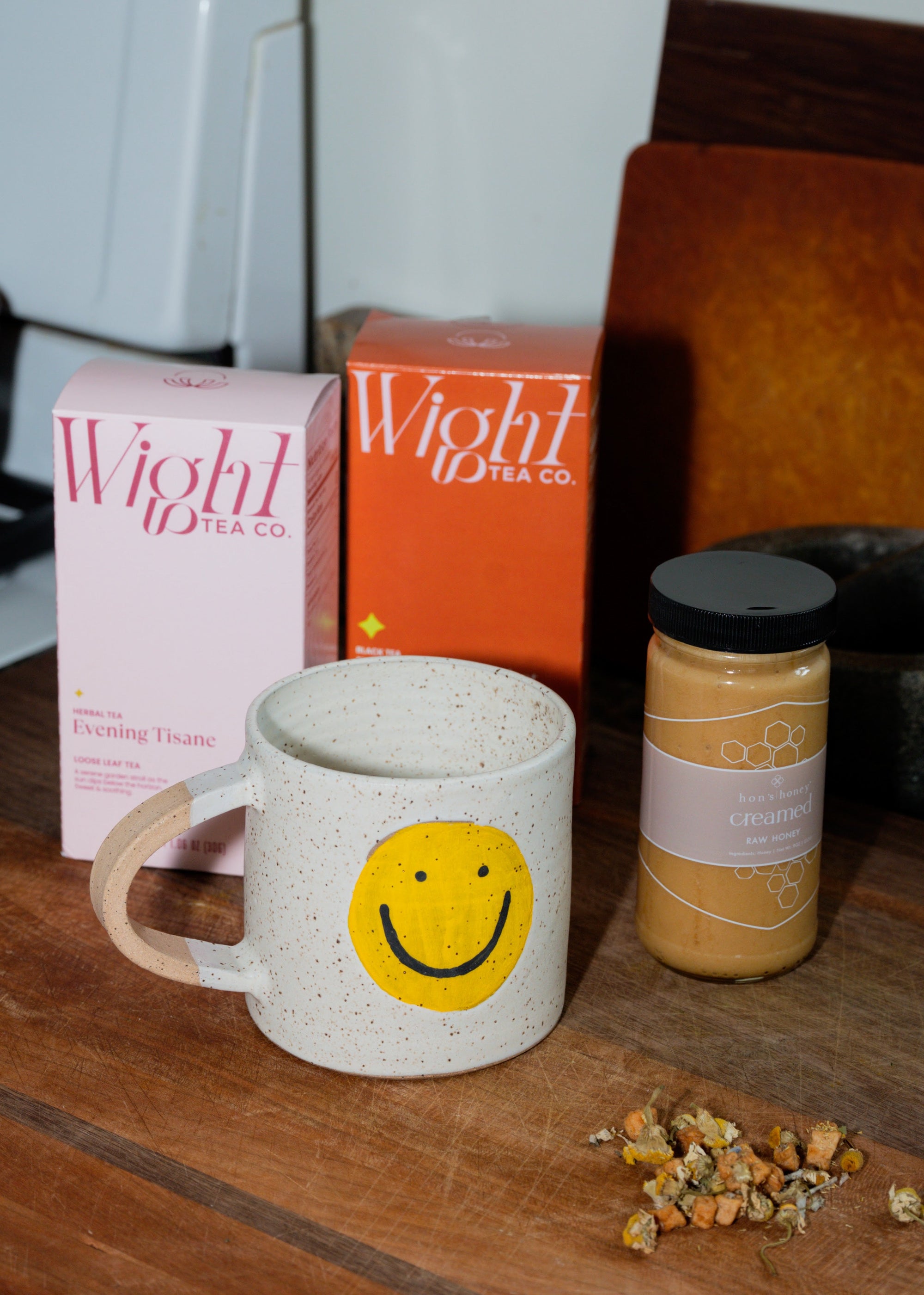 Smiley face mug with Wight Tea Co. tea boxes and a jar of Hon's Honey on a kitchen counter.