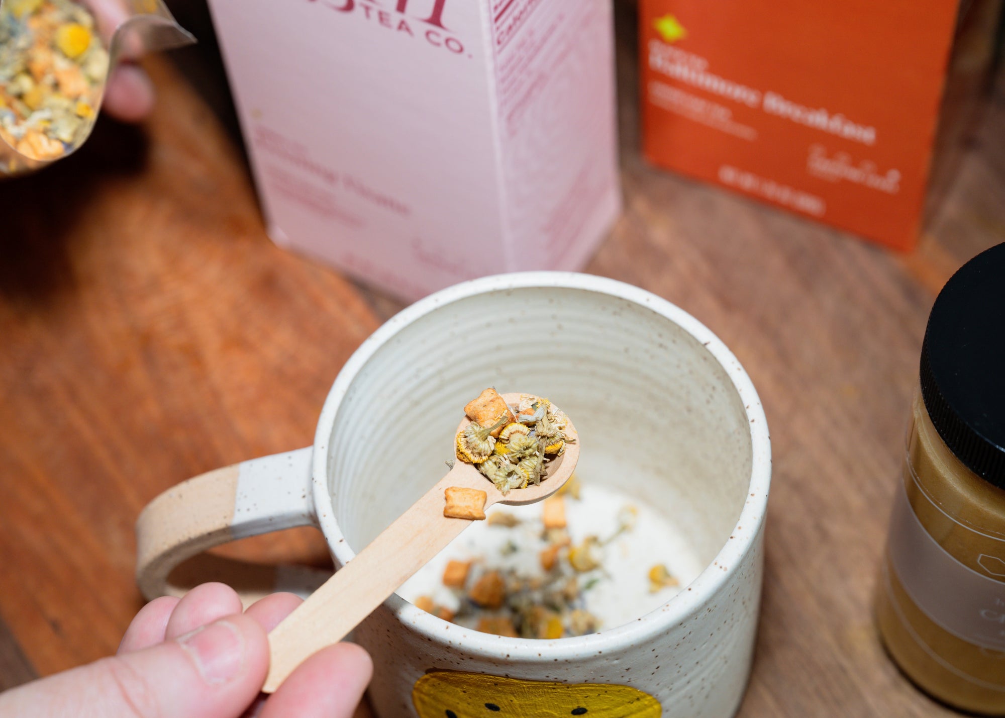 Person adding dried loose leaf tea to a mug with a wooden spoon.