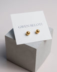 Gold woven ball earrings by Gwen Beloti displayed on a concrete block.