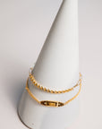 Two gold bracelets on a white cone-shaped stand against a light gray background