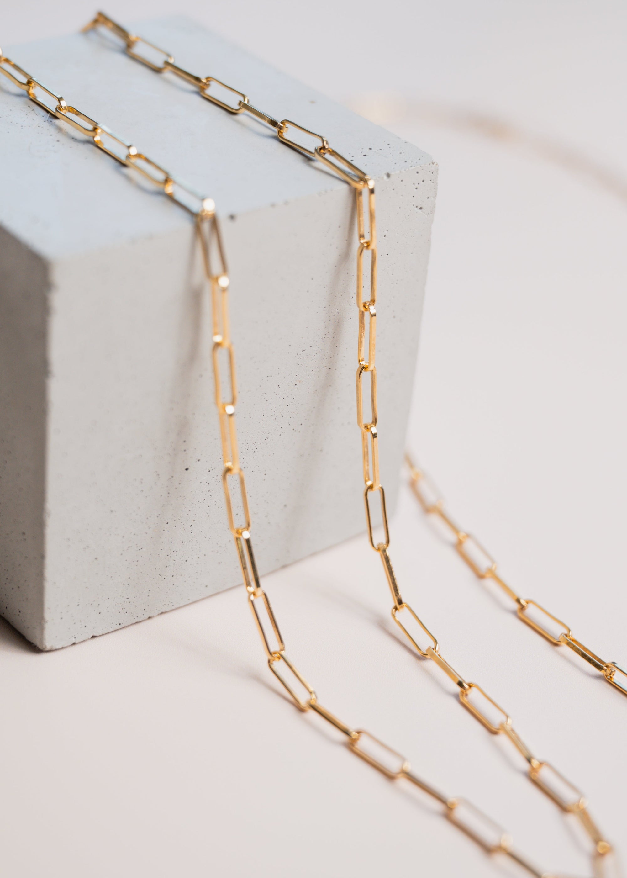 Close up of gold link chain necklaces by Gwen Beloti layered over concrete block display