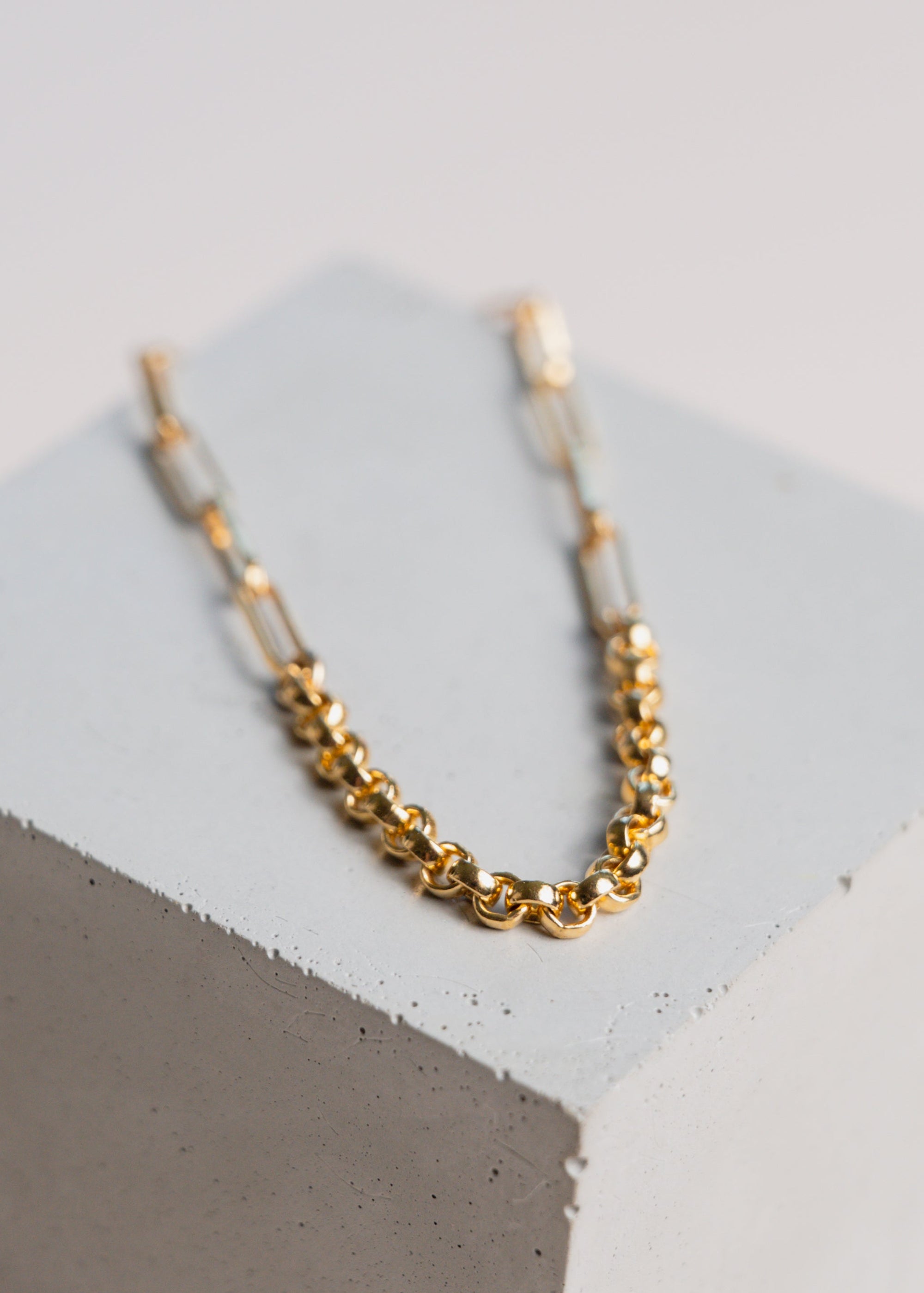 Gold two chain bracelet on a concrete block with pale background