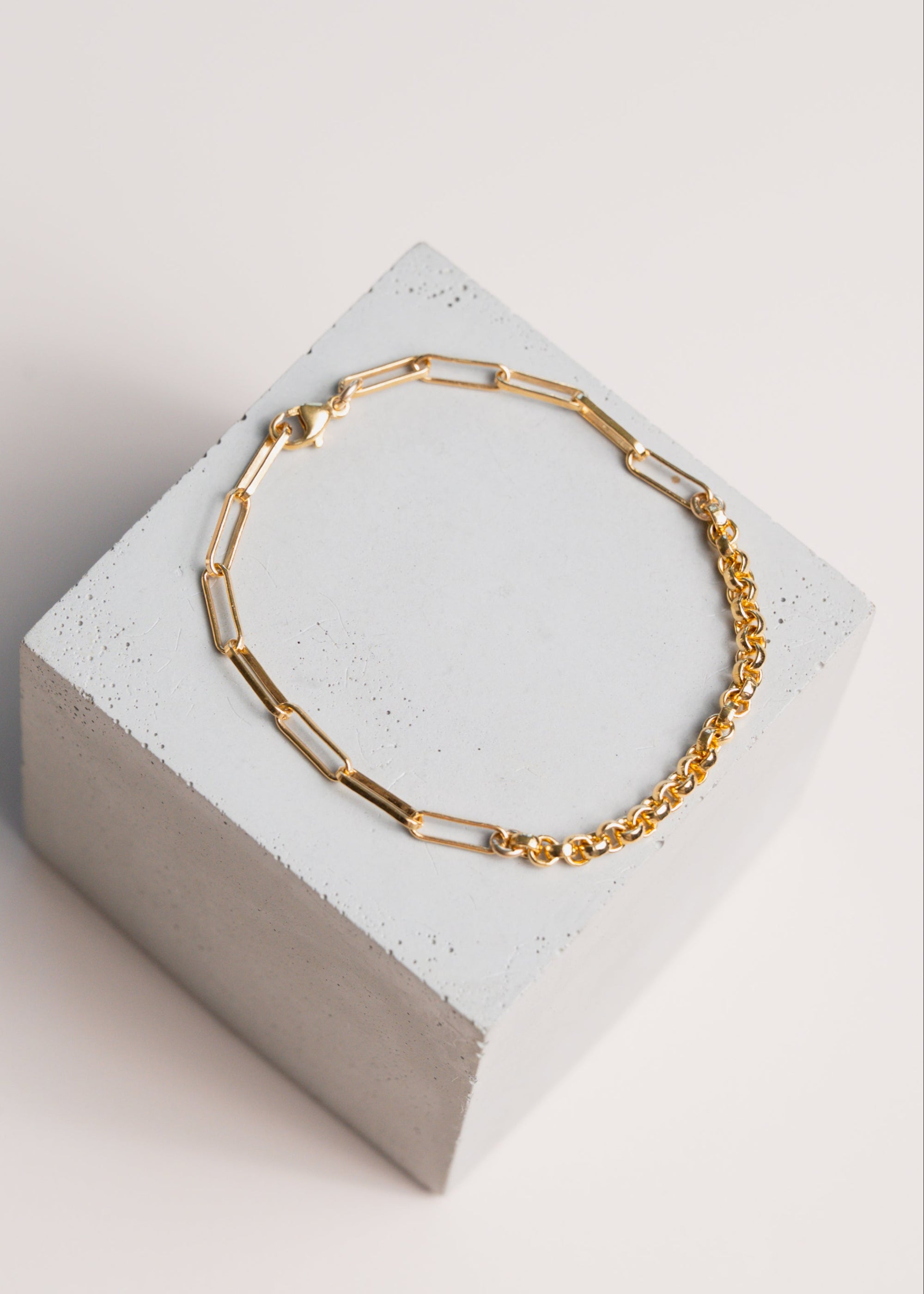 Gold two chain bracelet on a concrete block with pale background