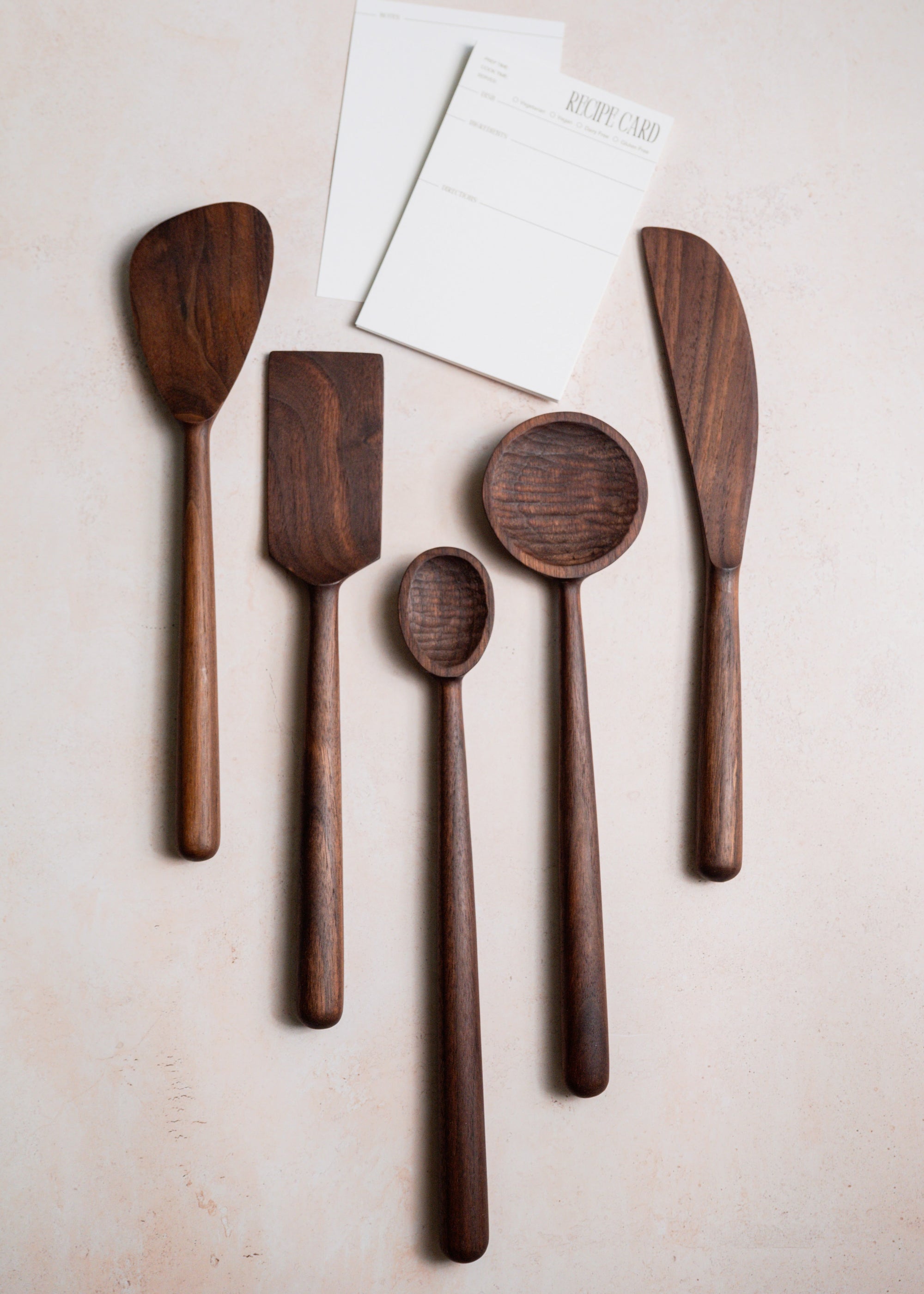 Set of walnut wooden kitchen utensils including spatulas and spoons on a light background
