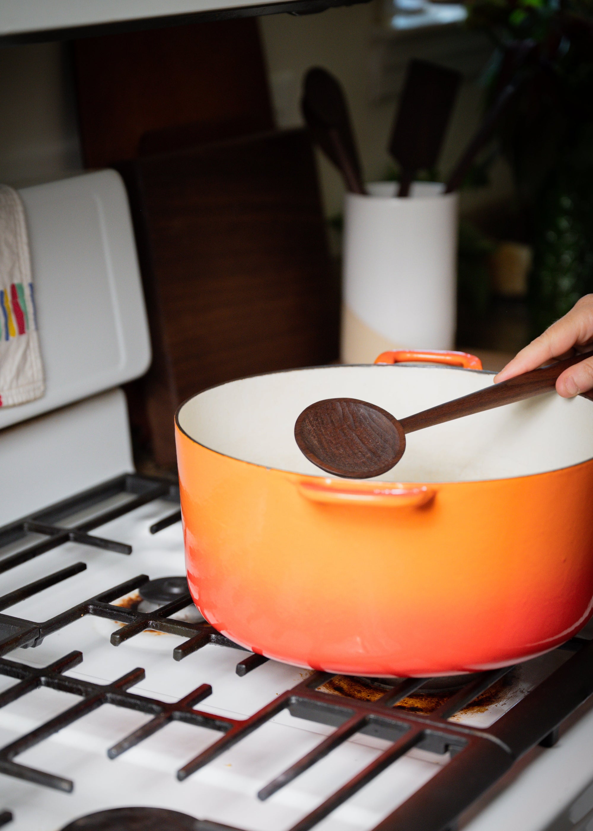 Walnut hand carved wooden spoon shown in use with a vintage orange Le Crueset cast iron pot