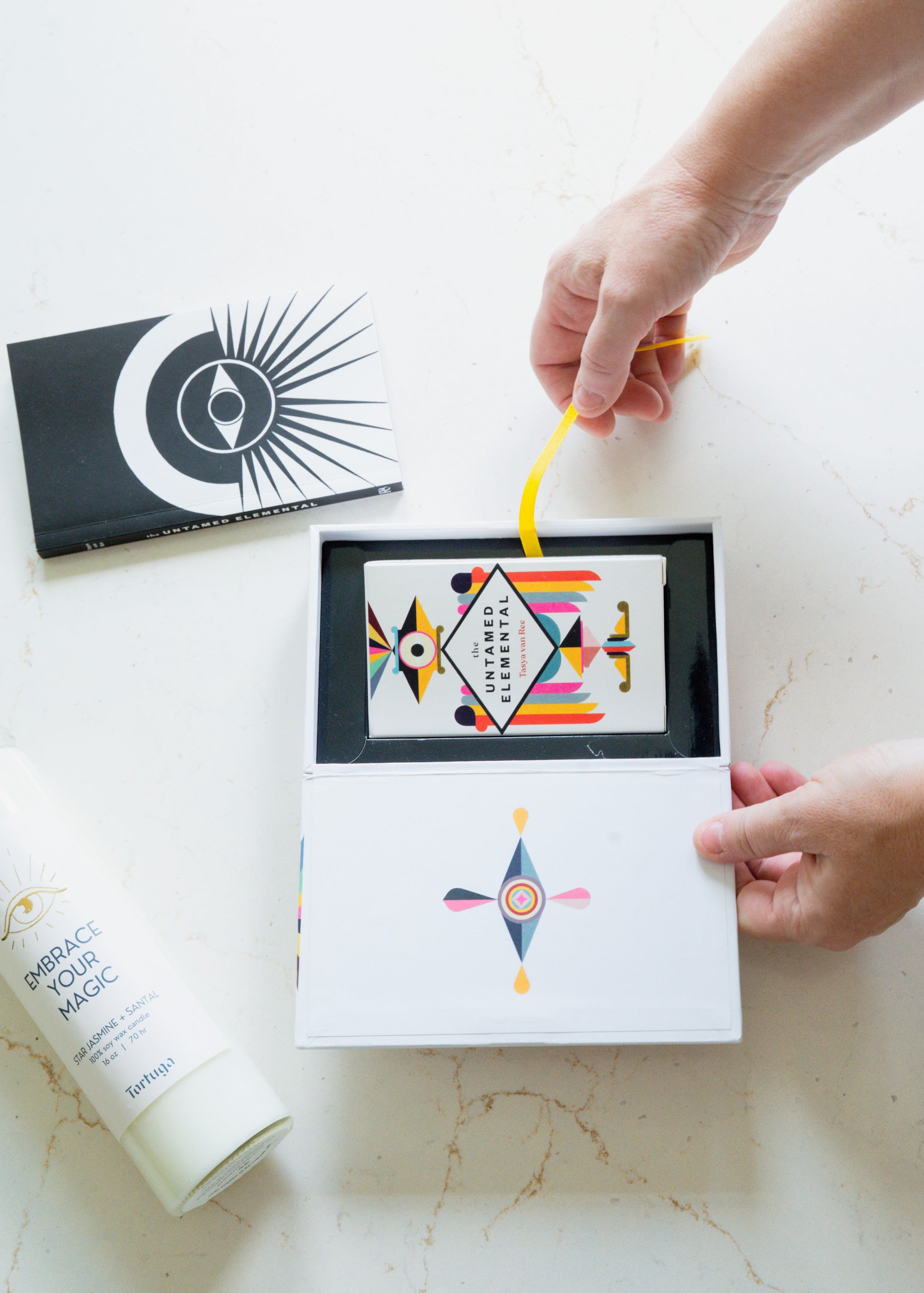 Person opening an oracle deck box with colorful geometric designs on a white surface