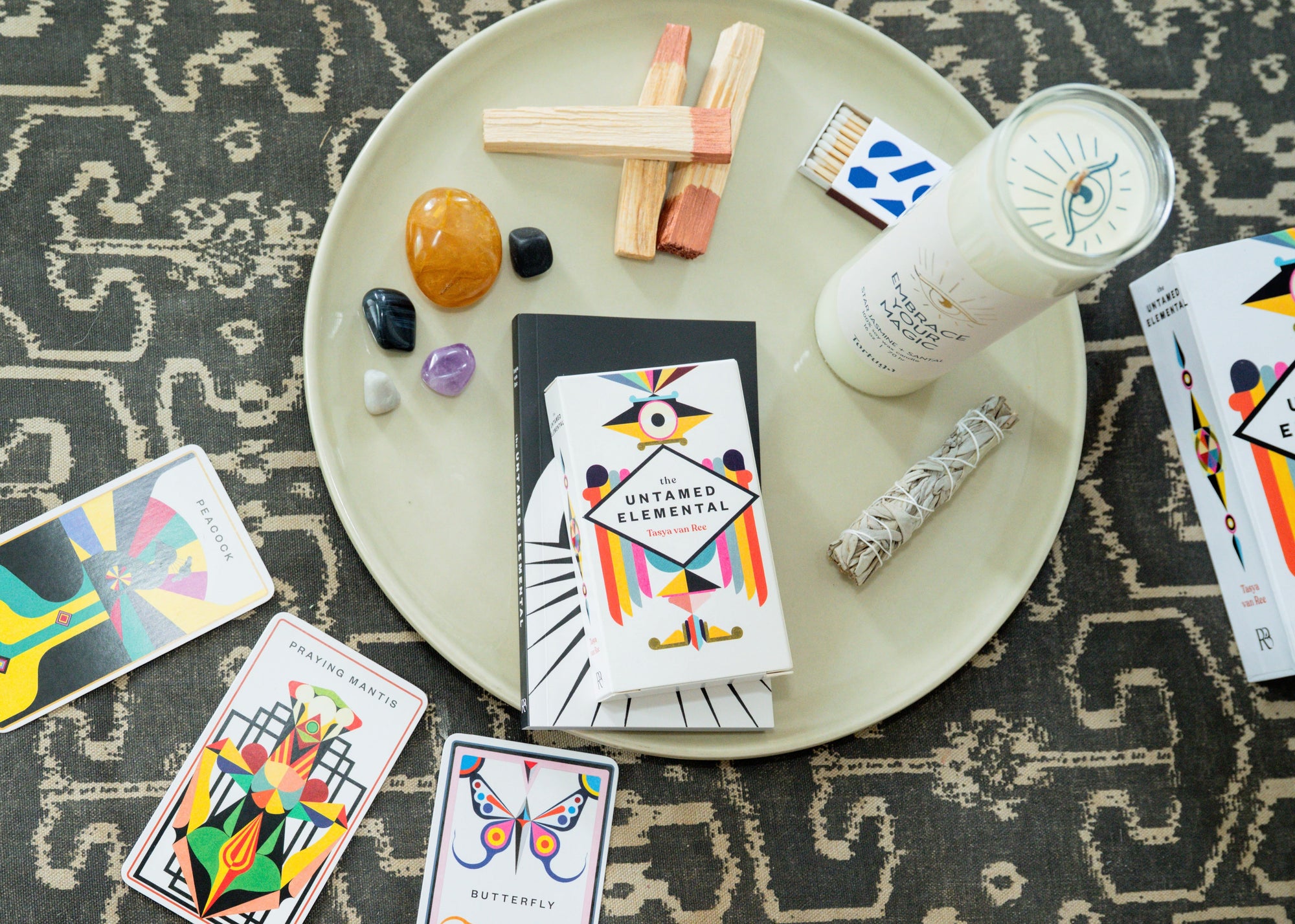 Colorful oracle cards, prayer candle, palo santo, sage and matches on a dish.