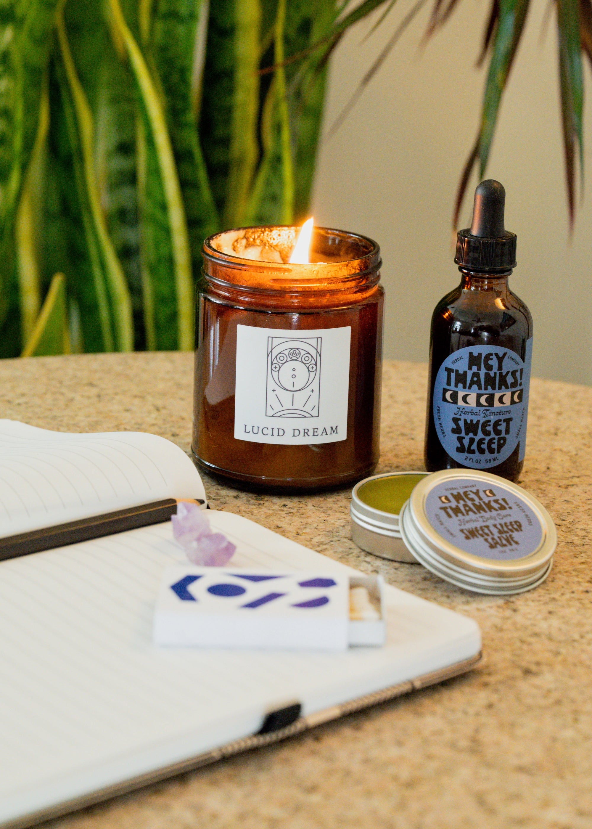 Collection of items including a notebook, candle, tincture, salve and matches on a table. 