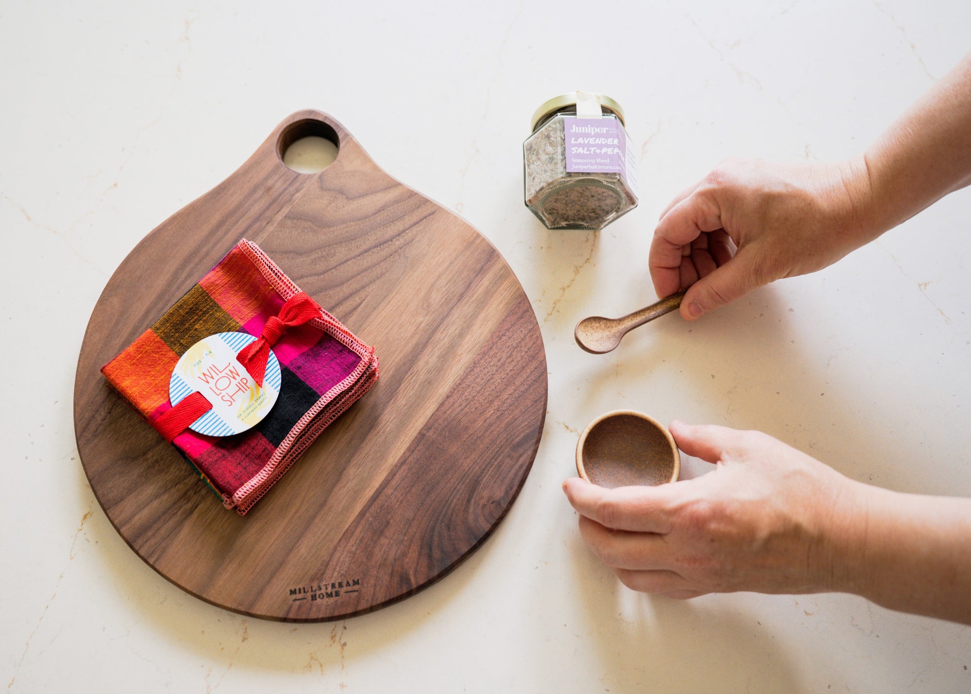 Wooden cutting board with colorful napkins, jar of salt and a small ceramic bowl and spoon on a table.