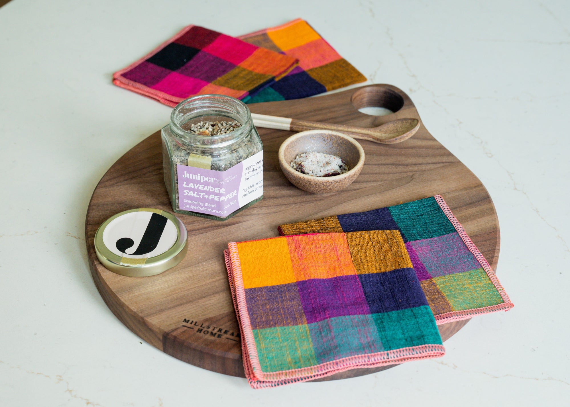 Colorful checkered napkins on a wooden serving board with a jar of salt and small bowl.