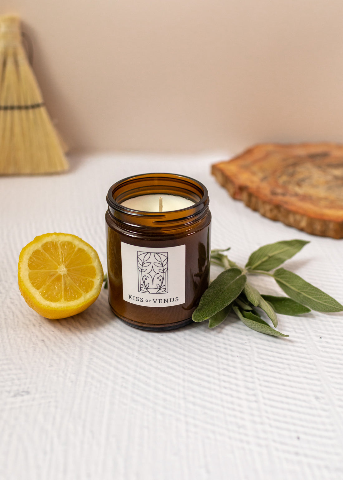 candle with label stating "kiss of venus" with sage sprigs and a lemon besides the candle