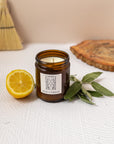candle with label stating "kiss of venus" with sage sprigs and a lemon besides the candle
