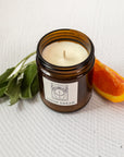 close up of a candle labeled "lucid dream" with orange slices and sage besides the candle on a white background