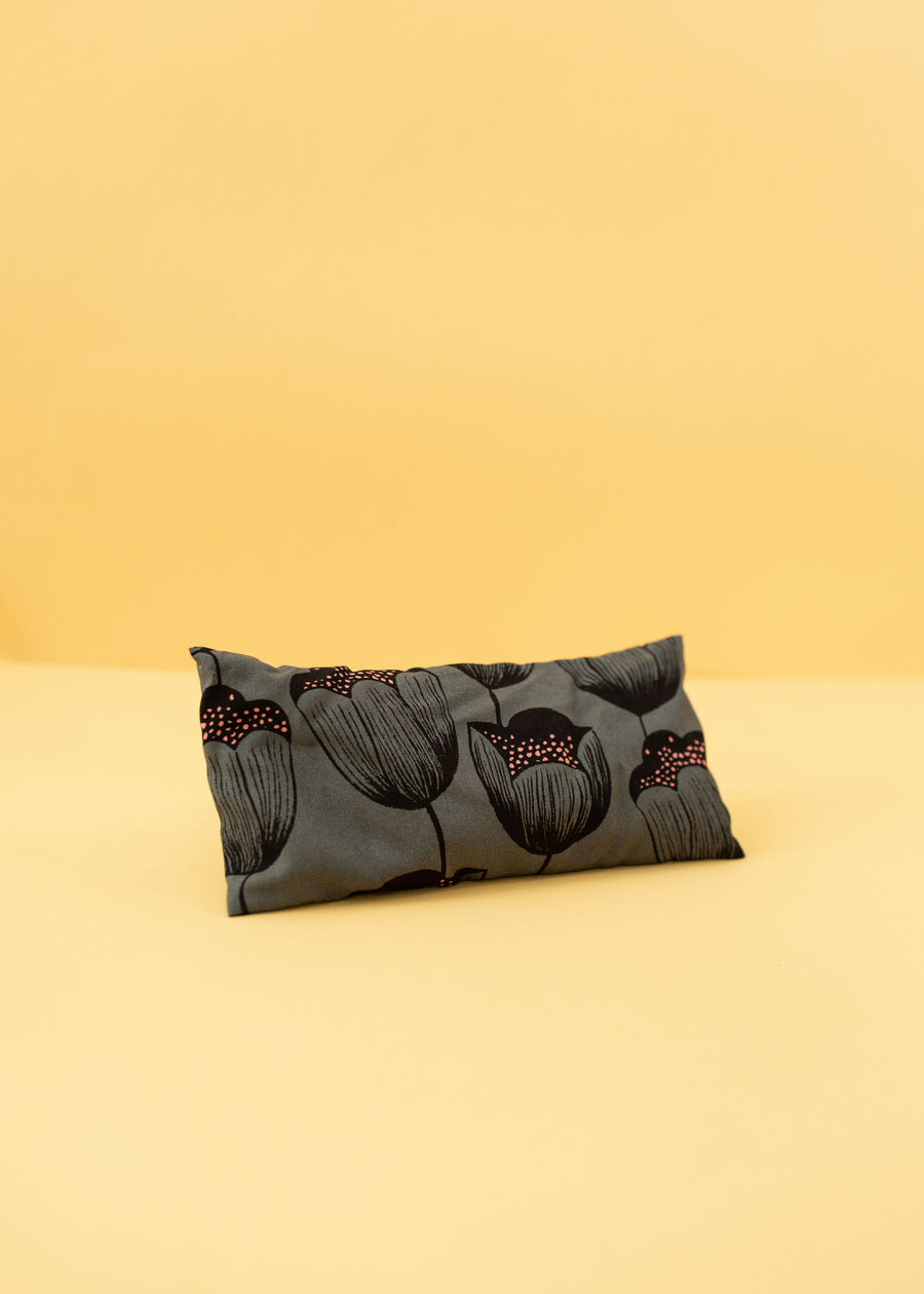 Gray eye pillow with black lined roses and specs of pink inside the flower