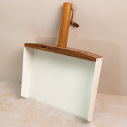 photo of a white large dust pan with a walnut handle, leaning against a pink background