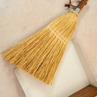 photo of a hand broom laying on a faint pink background with a white dust pan underneath