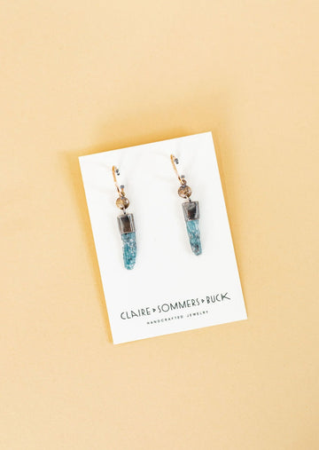 Two sister earrings from Claire and Sommers Buck with sterling silver hoops and kyanite crystals hanging down jewelry card