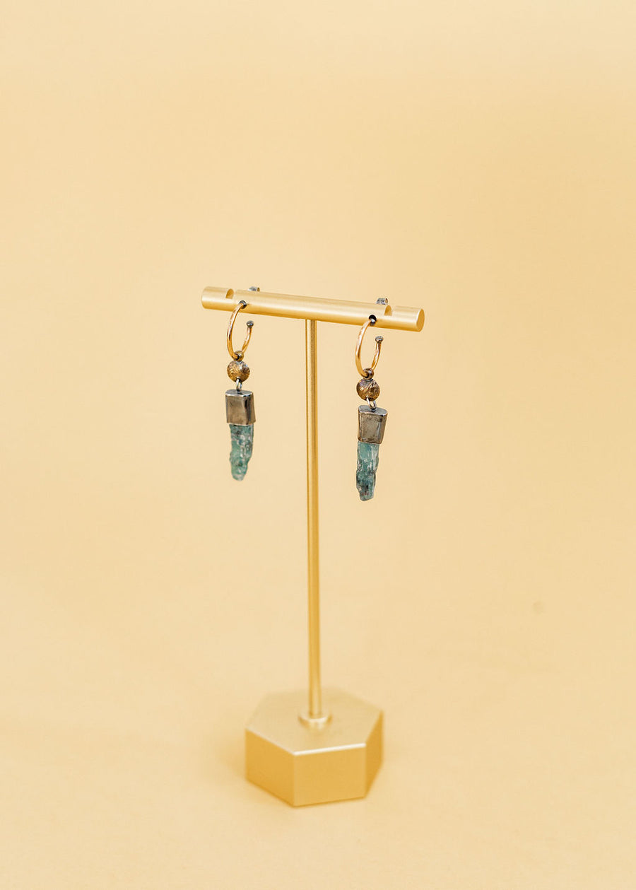 Two sister earrings from Claire and Sommers Buck with sterling silver hoops and kyanite crystals hanging down earring stand