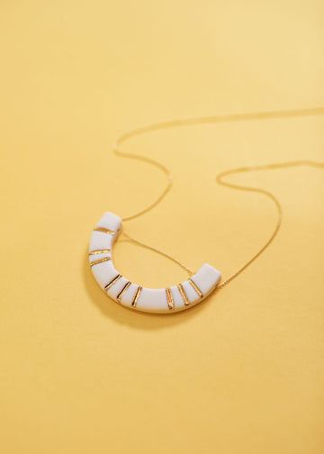 Close-up of arched shape structure on the end of a neckalce with a dainty band. The arch is white with various gold lines running through.