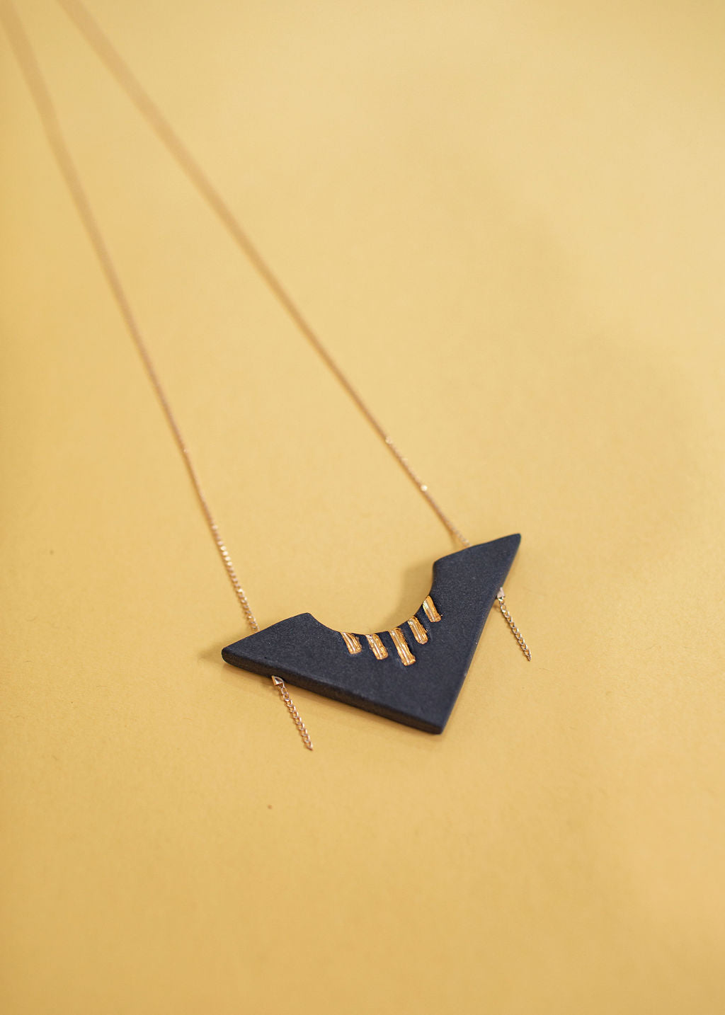 Photo of a obsidian necklace with a dainty gold chain attached. Porcelain pendant in the shape of an arrow with gold glaze accents on the top. 