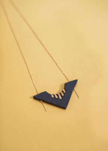 Photo of a obsidian necklace with a dainty gold chain attached. Porcelain pendant in the shape of an arrow with gold glaze accents on the top. 