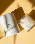flatlay of 'air' candle with yellow background. Candle is in light blue tinted glass with a 'n' shape in light gold on the front, sitting next to the case it comes in 